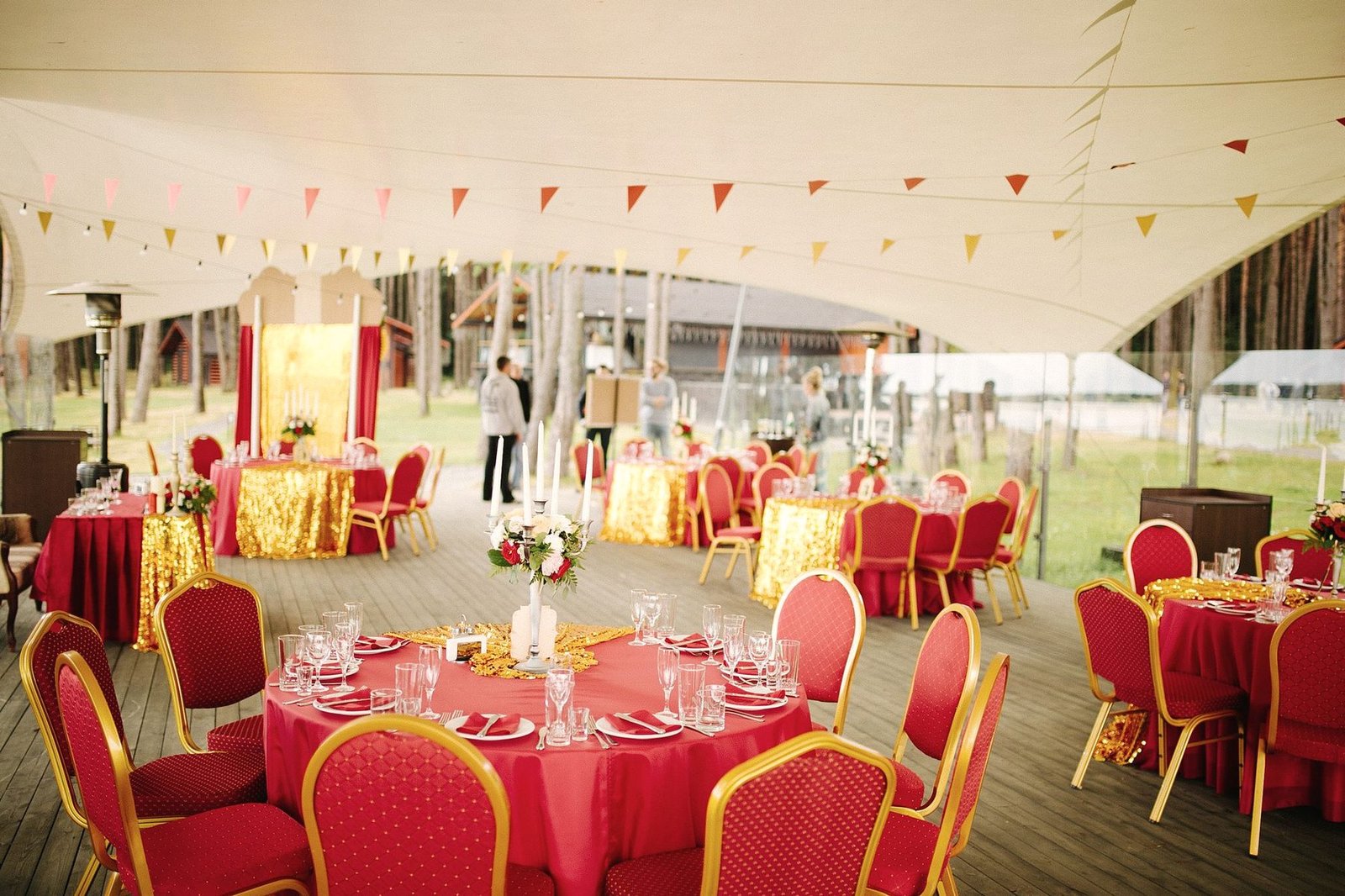 The inside of a marquee filled with round tables, red chairs and bunting.