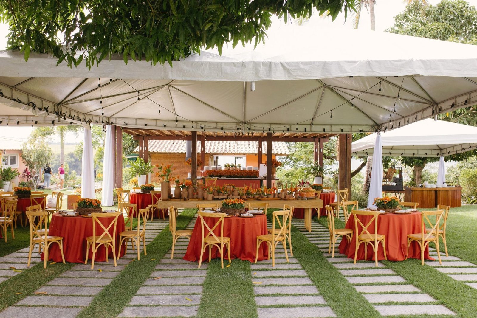 An outdoor reception laid out with round tables, red cloths and a canopy walkway.