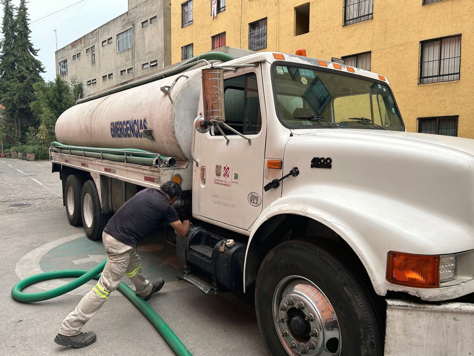 A white tanker truck parked at a kerb with an operator handling the suction hose.