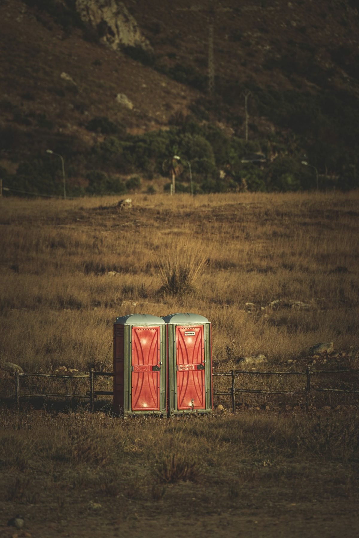 Two red portable toilet units alone on wide open grassland at dusk.