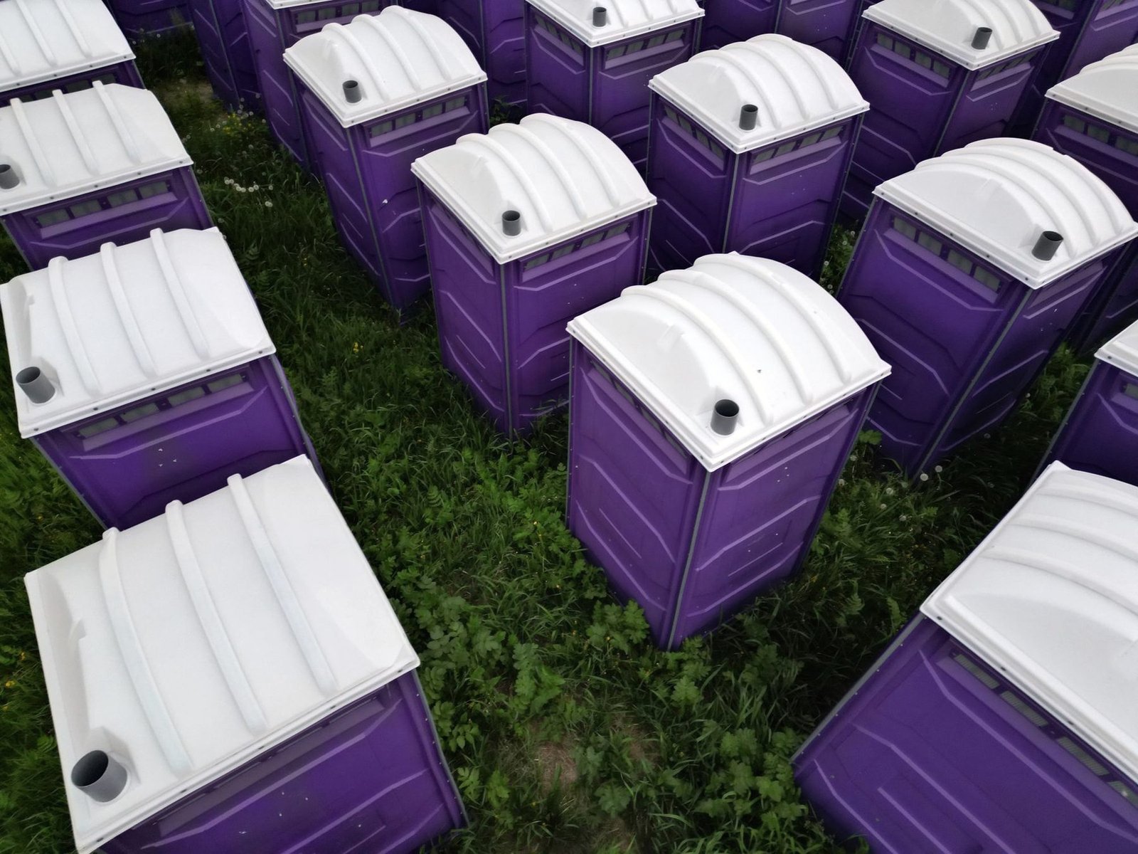 Purple and white portable toilet units seen from above, staged in rows on grass.